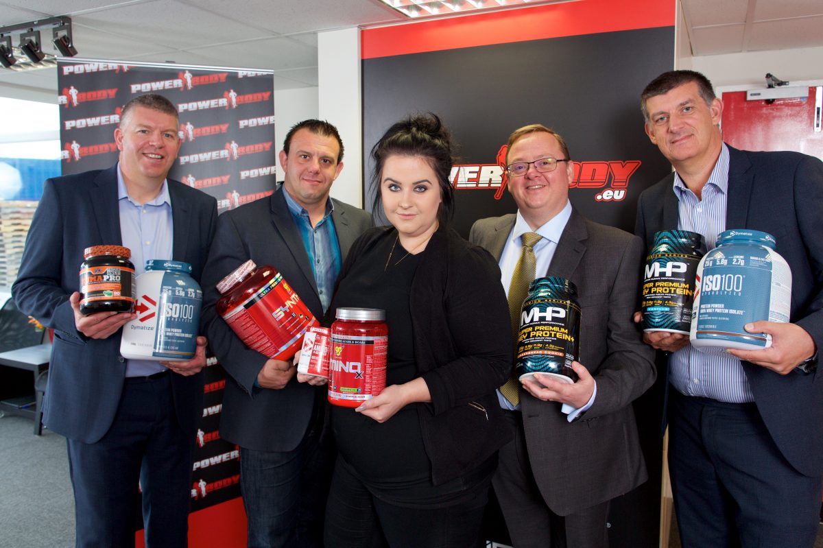 Four men and a woman holding large plastic canisters of product in an office.