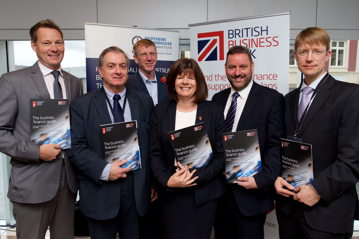 Five suited men and a woman standing around point of sale holding brochures in an office.