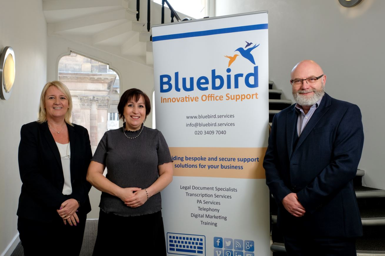 Two women and a man standing alongside a large poster stating Bluebird Innovative Office Support.