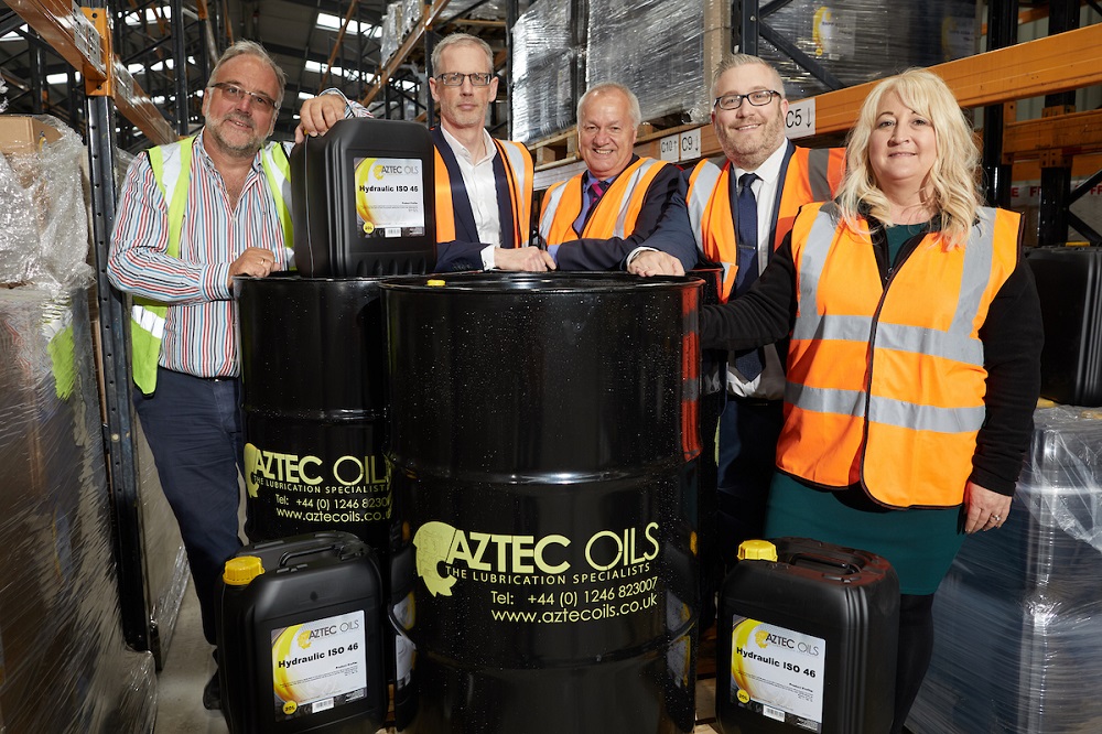 Five people in a factory standing next to Aztec Oils drums. One woman and four men are wearing Hi Vis jackets.