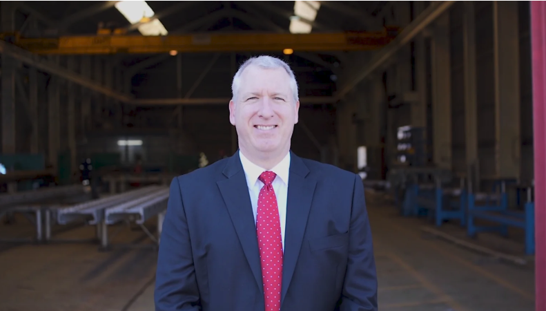 Man standing inside an empty warehouse wearing a blue suit and red spotted tie.