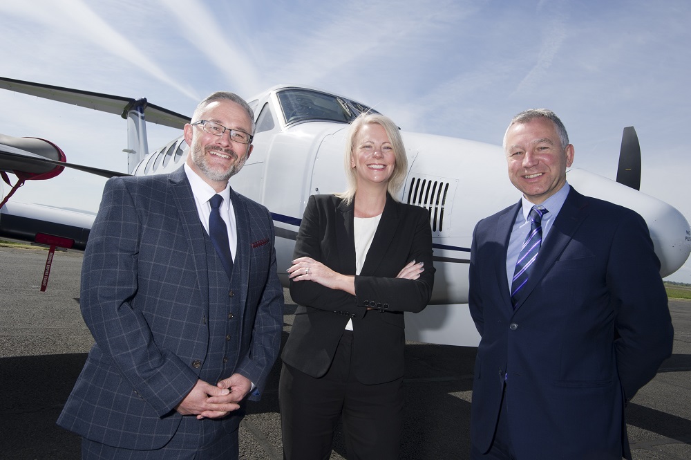 Two businessmen and business woman in the middle of the group standing in front of a small private aeroplane.