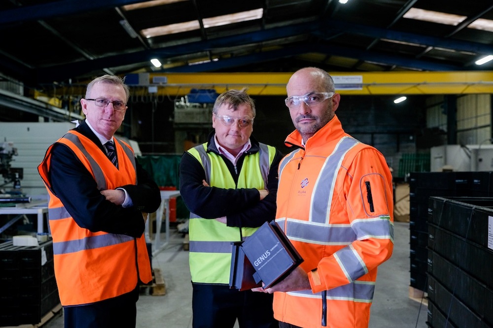 Two men in orange Hi Vis and a man in the middle of the row wearing yellow Hi Vis. There are situated in a factory.