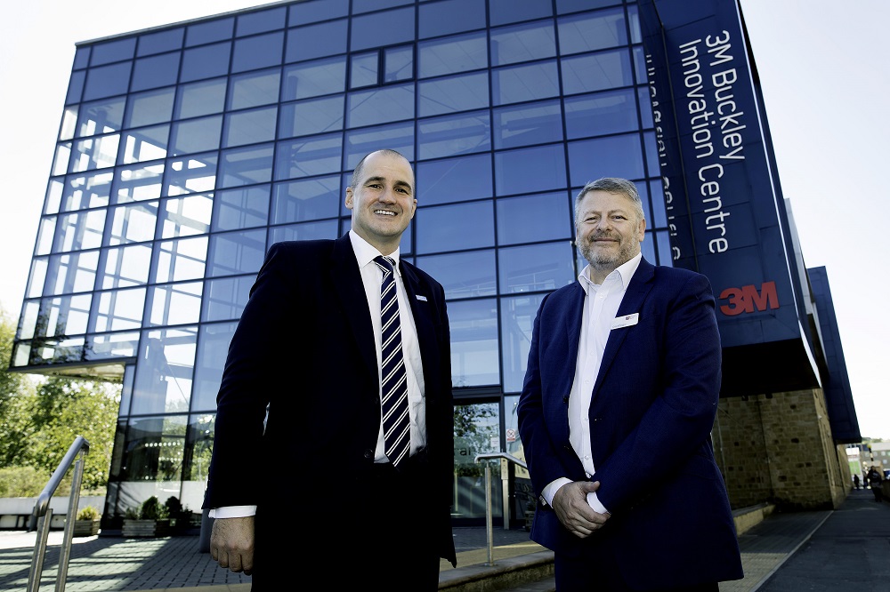Two men standing outside the 3M Buckley Innovation Centre. Man to the right has grey hair and is wearing a blue suit with a white shirt and the other man is nearly bald and is wearing a black suit, white shirt and blue stripey tie.