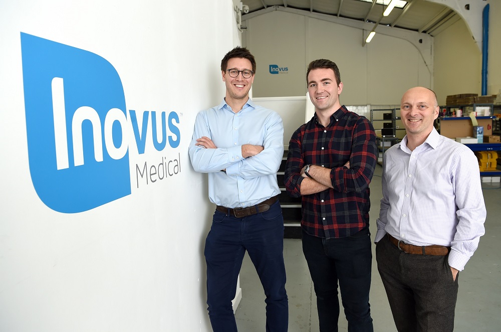 Three men standing in factory. Man to far left is leaning against Inovus Medical branded wall.