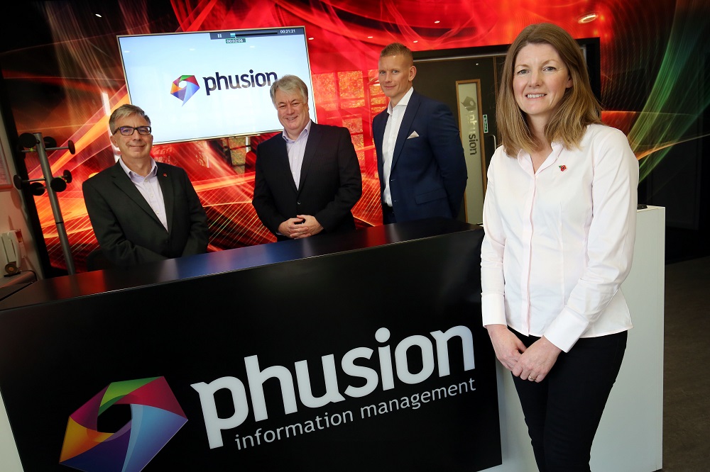 Three men wearing black suits and a woman wearing white shirt and black trousers standing in a room with Phusion Information Management point of sale.
