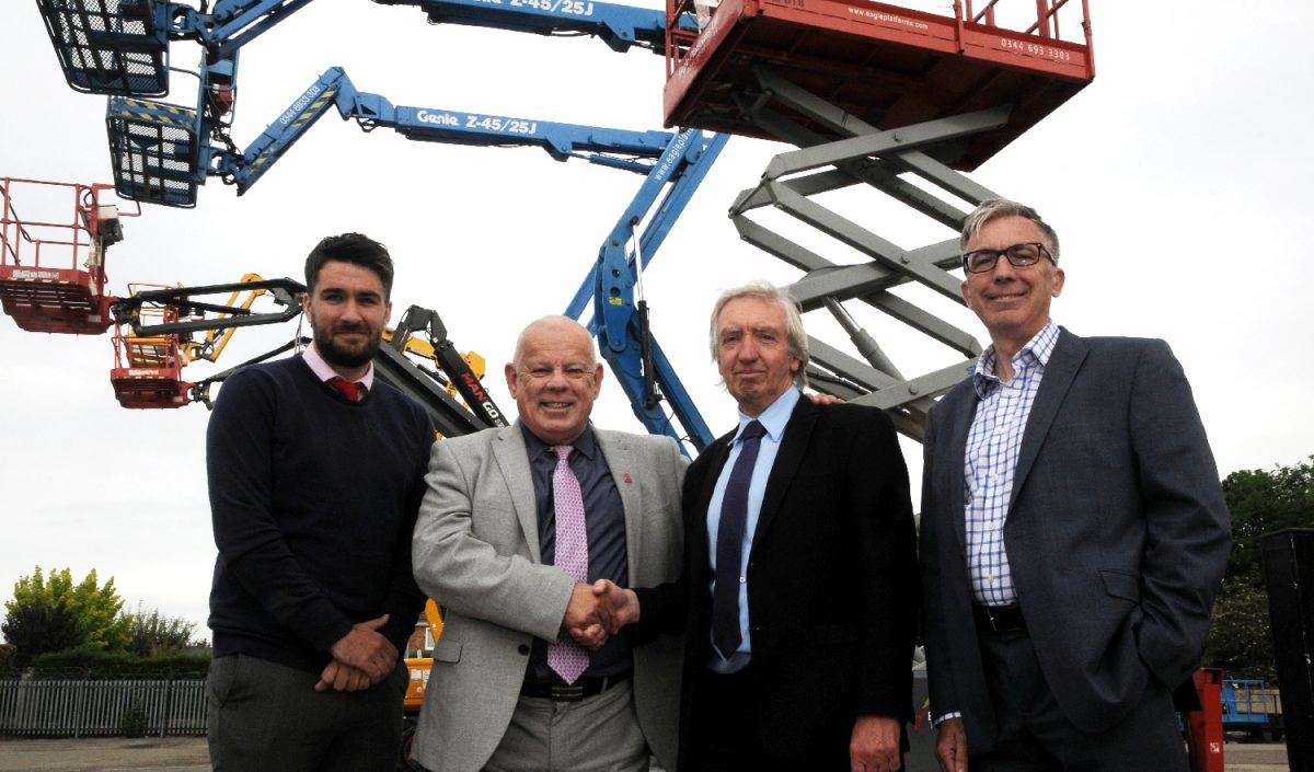 Four men outside standing in front of a large crane.