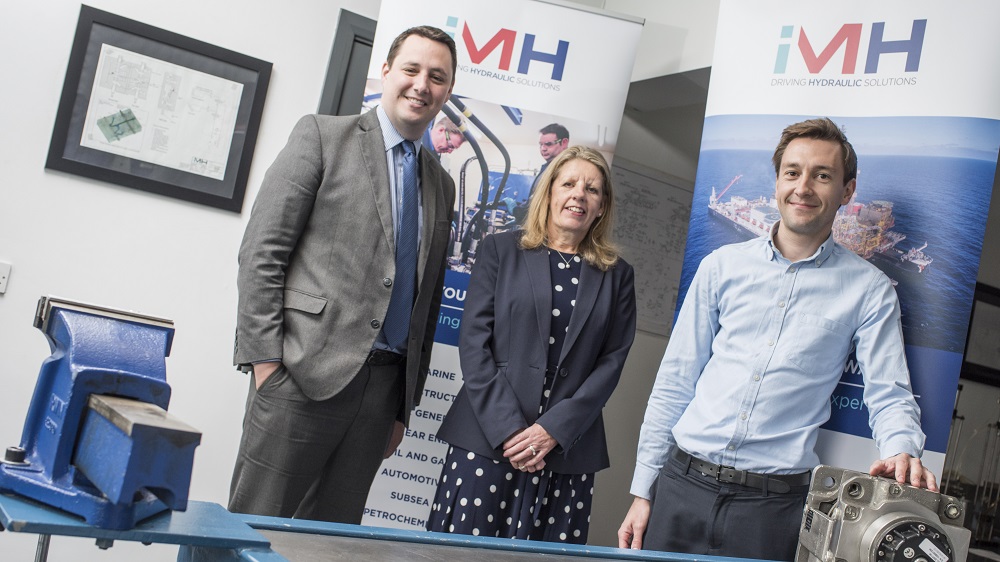 2 men and a woman stood in a meeting room with IMH Driving Hydraulic Systems pop up banners in the background