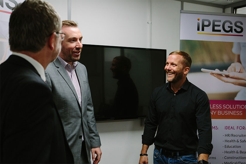 3 men from iPEGS talking in a meeting room with an iPEGS pop up banner in the background