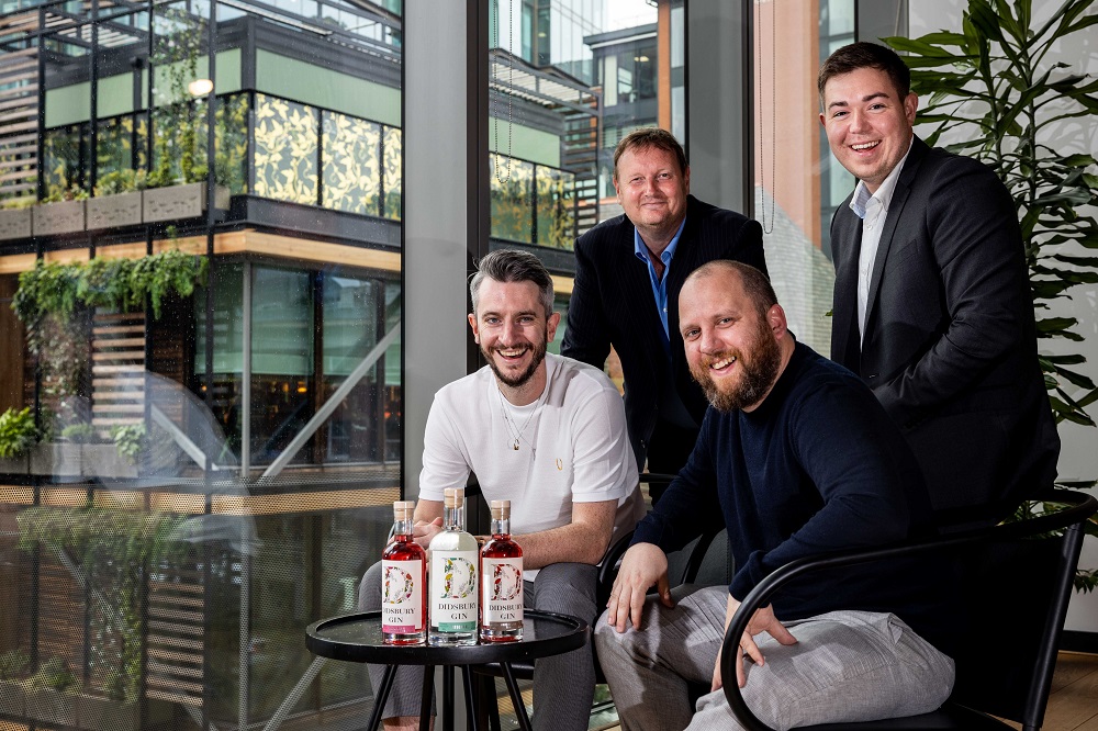 4 men gathered around a small table by a window in an office building showing Didsbury Gin