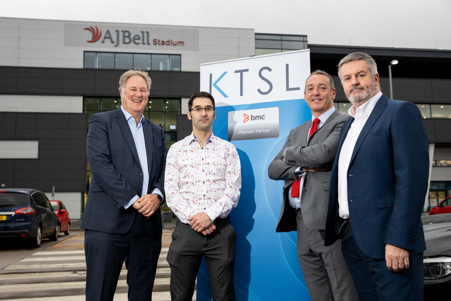 4 men stood outside of the AJ Bell Stadium with a KTSL pop up banner in the background