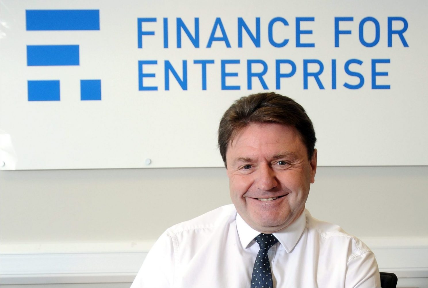 A man smiling and sat in front of a Finance For Enterprise wall sign