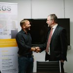 2 men shaking hands in a meeting room with iPEGS pop up banners beside them