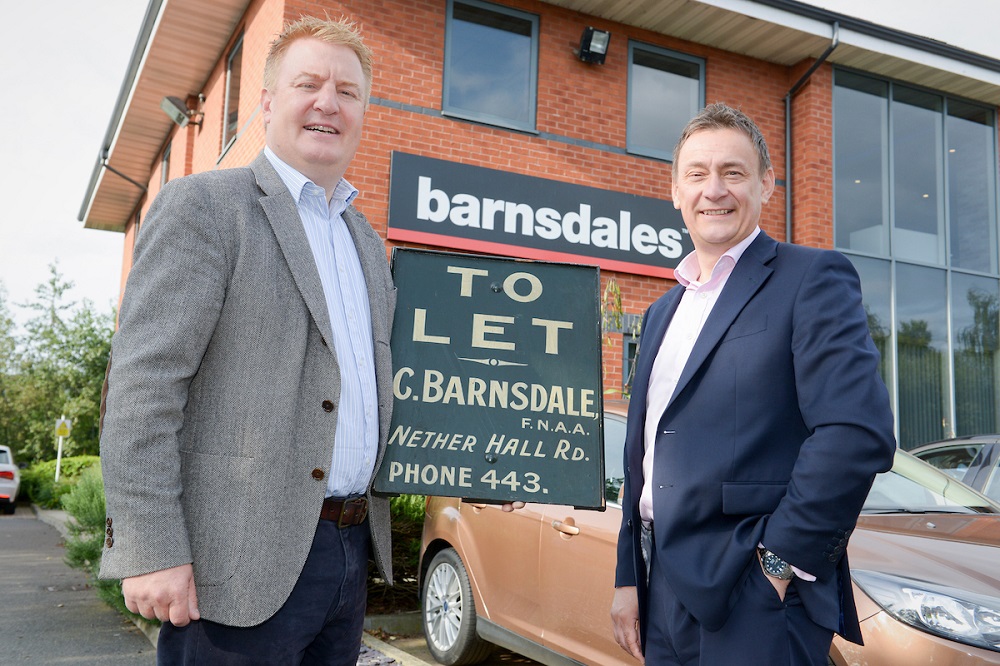 Two men standing outside office with Barnsdales signage on building. Man to the far right is wearing a blue suit with a pink shirt and taller man to the left is wearing a grey jacket, blue shirt and a navy trousers.