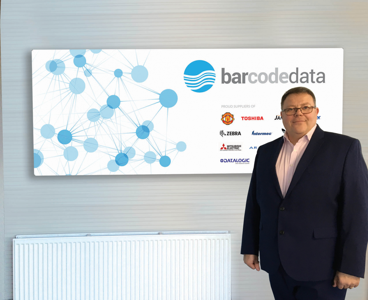 A man standing in front of Bar Code Data sign on a wall