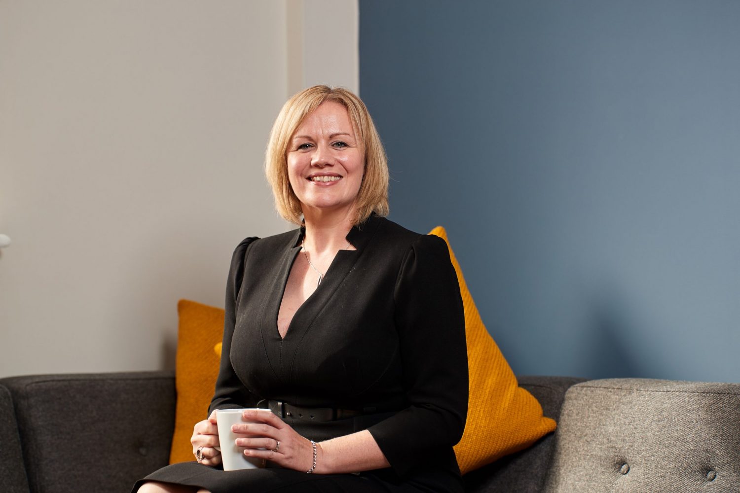 Joanne Whitfield, Fund Director at FW Capital sitting on a couch holding a mug