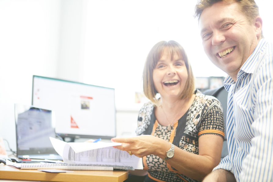 A man and a woman sat at an office desk laughing