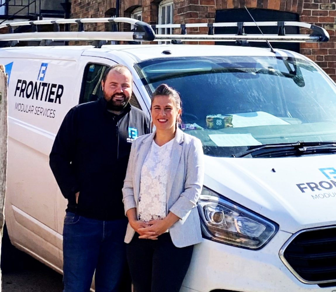 A man and woman smiling and stood in front of a Frontier Modular Services van