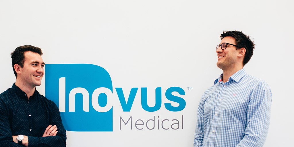 2 men from smiling and looking at each other in front of an Inovus Medical branded wall